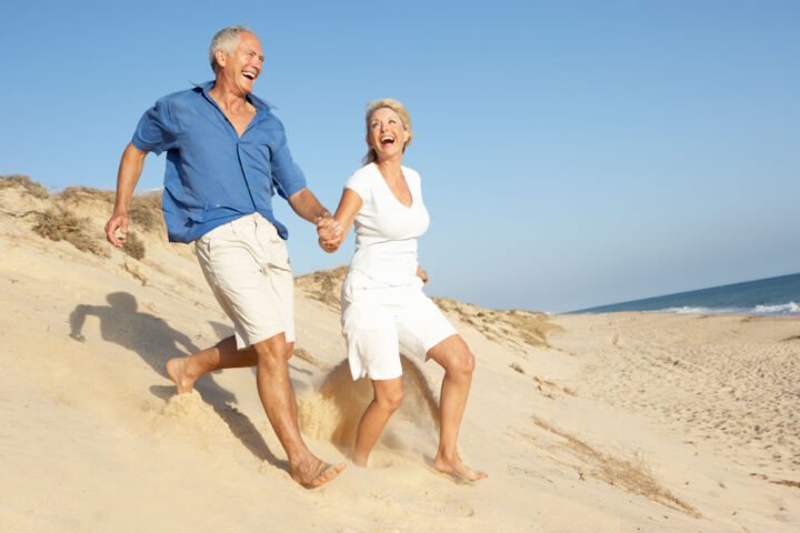 senior couple holding hands running on beach celebrating Health Benefits to Aging in Place